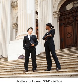 A professionally dressed woman and man outdoors on the steps of a legal or municipal building. Could be business or legal professionals or lawyer and client. - Shutterstock ID 2341467603