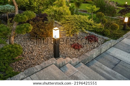 Professionally Landscaped Backyard Garden Illuminated with Outdoor Bollard Lamps Installed Along the Path in the Tree Bark Mulch.