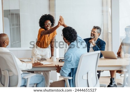 Professionals celebrate their achievements with a high five, promoting teamwork and success in this creative startup environment. Business people collaborating in a vibrant office setting.
