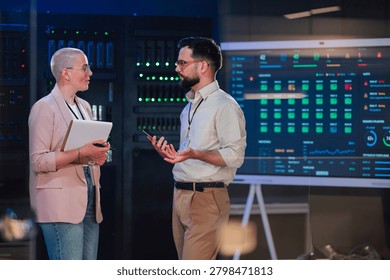 It professionals collaborating in a data center, analyzing system performance on a large screen, ensuring robust cyber security
