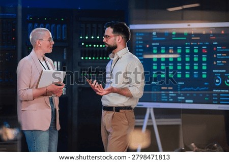 It professionals collaborating in a data center, analyzing system performance on a large screen, ensuring robust cyber security