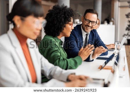 Professionals collaborating in an office, showcasing teamwork and discussion in a business environment. Optimistic and productive interaction among colleagues seated at desks with laptops.