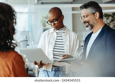 Professionals in a corporate setting demonstrate teamwork and cooperation while engaging in a productive discussion. Group of business people having a standup meeting with a laptop in an office. - Powered by Shutterstock