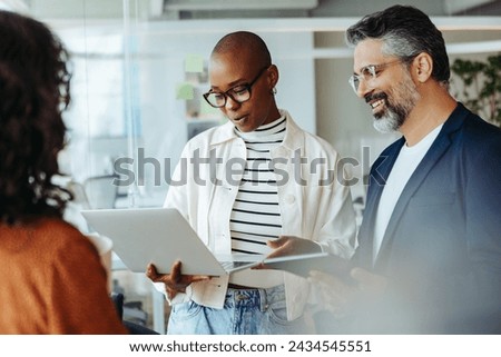 Professionals in a corporate setting demonstrate teamwork and cooperation while engaging in a productive discussion. Group of business people having a standup meeting with a laptop in an office.