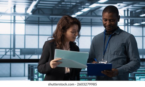IT professionals in data center reviewing reports and files, crosschecking network performance metrics and security logs. Server room workers doing troubleshooting to prevent downtime, camera A
