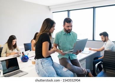 Professionals discussing over laptop while sitting with colleagues at desk 
