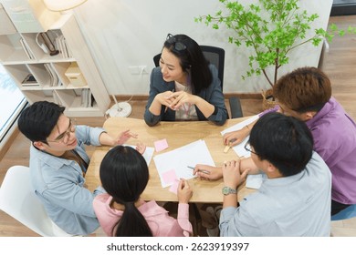 Professionals engage in a collaborative brainstorming session at a modern office. They share ideas, write on sticky notes, and discuss strategies around a wooden table in a relaxed atmosphere.