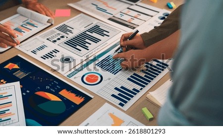 Professionals engage in a collaborative effort over various business charts and reports, focusing on data analysis and strategic planning in a modern office environment. SACTR