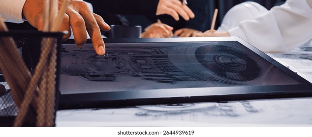 Professionals engage in a collaborative engineering project, using a digital tablet and blueprints. The environment showcases innovation and teamwork in design processes. SACTR