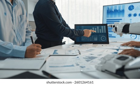 Professionals engage in data analysis with digital displays and documents in a modern office space, utilizing advanced technology for effective collaboration.Noogenesis