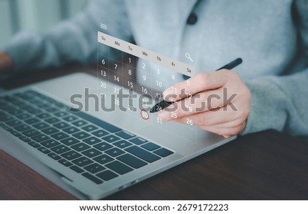 A professional's hand is using a stylus, pointing to a virtual calendar projected over a laptop, with a specific date circled. Concept for efficient digital planning, time management, and deadlines.