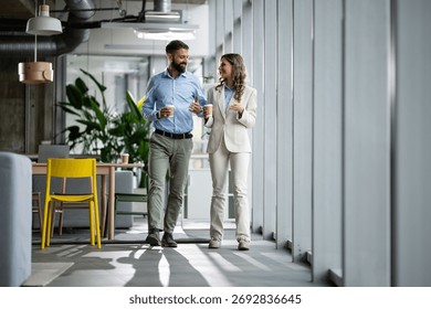 Professionals having a discussion while walking through a modern office corridor, holding disposable coffee cups