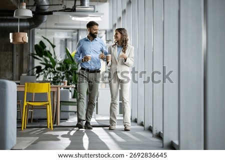 Professionals having a discussion while walking through a modern office corridor, holding disposable coffee cups