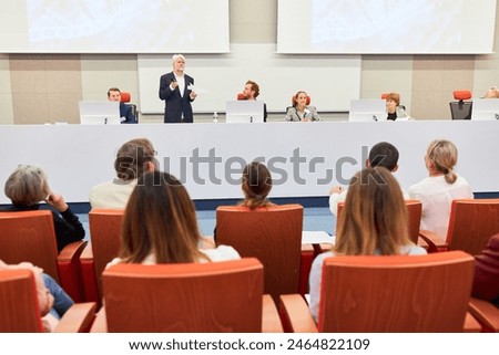 Professionals sitting at audience in front of panel during business conference in auditorium