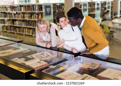 Professor And Adult Students Read Ancient Books In A Library Showcase. High Quality Photo