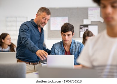 Professor assisting college student with laptop in classroom during computer lesson. Teacher talking and explaining to guy. Mature man lecturer helping high school teen with laptop during lecture. - Powered by Shutterstock