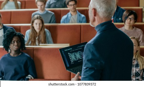 Professor of Computer Science Reads Lecture to a Classroom Full of Multi Ethnic Students. Teacher Holds Laptop with Deep Learning, Artificial Intelligence Infographics on the Screen.