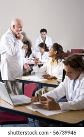 Professor With Medical Students Wearing Lab Coats In Classroom