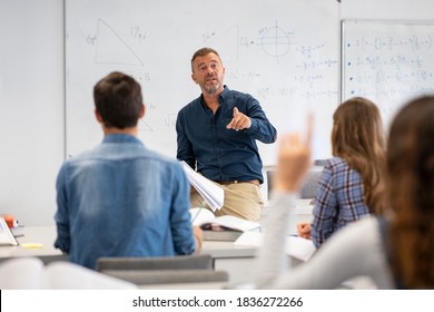 Professor pointing at college student with hand raised in classroom. Student raising a hand with a question for the teacher. Lecturer teaching in class while girl have a question to do during a lesson - Shutterstock ID 1836272266