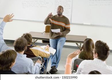 Professor Pointing At College Student With Hands Raised In Classroom