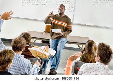 Professor pointing at college student with hands raised in classroom