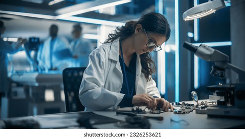 Proffesional Female Engineer Working on Electronic Circuit Boards. On Blurred Background Industrial Robotics Specialists in Lab Coats Working on a Mobile AI Robot in a Tech Factory Facility. - Powered by Shutterstock