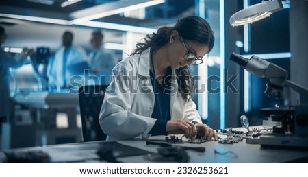 Proffesional Female Engineer Working on Electronic Circuit Boards. On Blurred Background Industrial Robotics Specialists in Lab Coats Working on a Mobile AI Robot in a Tech Factory Facility.