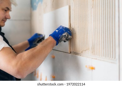 Proffesional tiler installing wall tile at home. Workers laying tiles on a bathroom wall. DIY, Do it yourself concept. House improvement. Repair renovation work. Selective focus, copy space