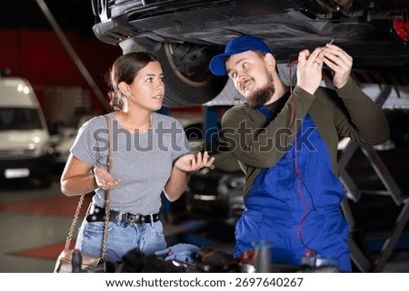 Proficient car mechanic checking operability of auto-element while female client watching him with upset look in auto repair shop