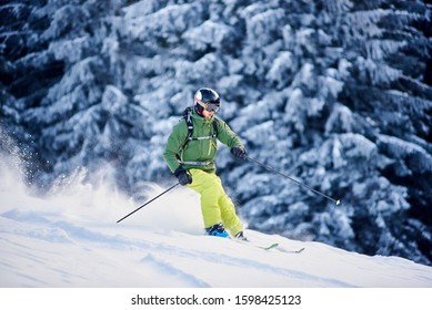 Proficient skier coming down along wooded hillside using professional ski equipment and making deep snow powder. Winter outdoors activities concept. Picturesque forest scenery on background. Side view - Shutterstock ID 1598425123