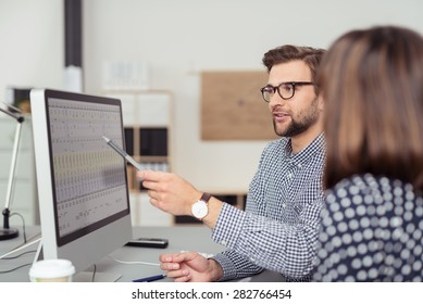 Proficient young male employee with eyeglasses and checkered shirt, explaining a business analysis displayed on the monitor of a desktop PC to his female colleague, in the interior of a modern office - Shutterstock ID 282766454