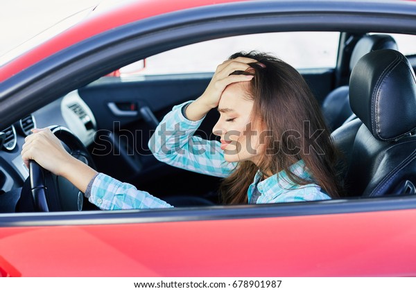 Profile of annoyed\
woman driving red car, stress while driving. Tensed woman leaning\
on hand with closed eyes, traffic jams. Head and shoulders of\
brunette woman inside\
car