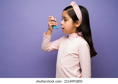 Profile of a beautiful child having respiratory problems and using an asthma inhaler against a purple background - Powered by Shutterstock