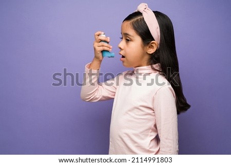Profile of a beautiful child having respiratory problems and using an asthma inhaler against a purple background