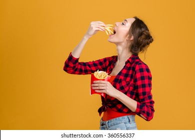 Profile of beautiful happy woman in plaid shirt tasting french fries over yellow background