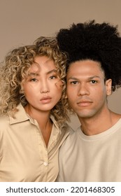 Profile of a biracial man in his 30's and a multiracial woman in her 20's looking at the camera on a neutral background. Stock Photo