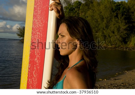 profile of a brunette woman standing next to a surfing board