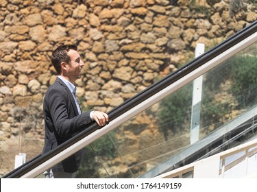 Profile Of A Businessman Climbing An Escalator In The Middle Of The Street And In Front Of A Stone Wall