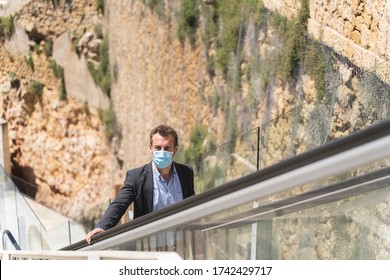 Profile Of A Businessman With A Face Mask On An Escalator In The Middle Of The Street And In Front Of A Stone Wall