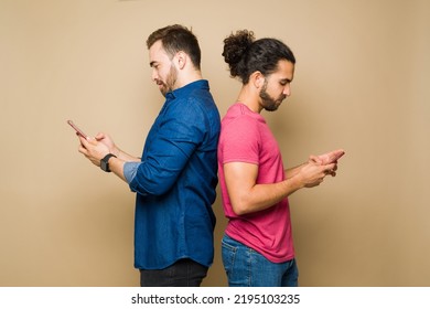 Profile Of A Caucasian Gay Man And Hispanic Boyfriend Standing Back To Back Texting On Their Smartphones