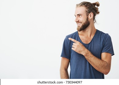 Profile of cheerful handsome man with fashionable hairstyle and beard smiling brightfully and pointing at free space for advertisement. - Shutterstock ID 730344097
