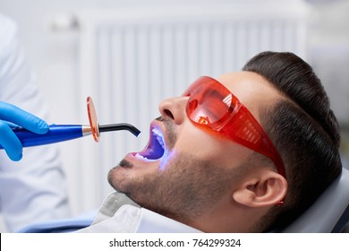 Profile close up shot of a handsome bearded man wearing protective glasses getting teeth filling done at his dental clinic copyspace technology ultraviolet UV lamp modern medicine health.