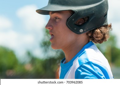 Profile of a curly haired teenage baseball boy close up in helmet during a game.