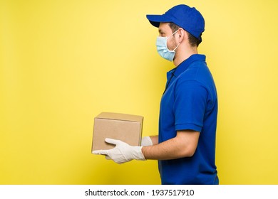 Profile Of A Delivery Courier With A Face Mask And Gloves Carrying A Small Package. Hispanic Man Working And Making A Delivery During The Coronavirus Pandemic