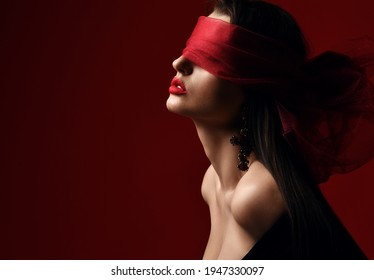 Profile of excited woman with naked shoulders and breast holds and eyes covered with red scarf, blindfold over dark background with copy space. Fashion, vogue, sexy stylish look for woman concept