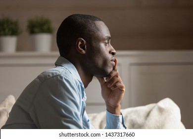 Profile face sad african guy in tension touch chin lost on thoughts thinking sit on couch in living room alone, try to make difficult decision, going through divorce or break up personal life problems - Powered by Shutterstock