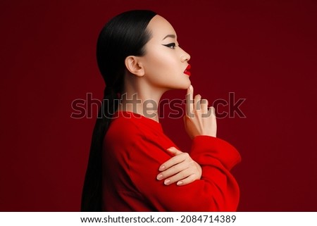 Profile fashion portrait of attractive asian model posing against red background