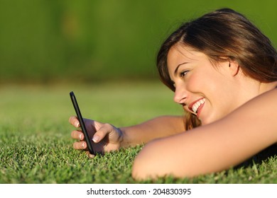 Profile Of A Funny Girl Using A Smart Phone On The Grass Of A Park With A Green Background