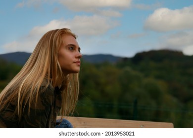 profile of a girl looking up, outdoors, with a beautiful blue sky behind the green mountains, think about her future or love