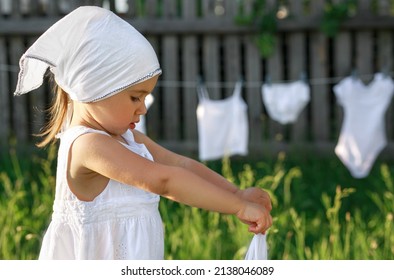 Profile of a girl in a white scarf washing clothes. A child squeezes wet underwear. Mom's little helper. T-shirts dry on a rope after laundry. Copy space